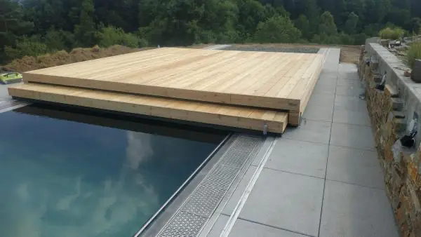 <p>Zde je vidět příkladná ukázka toho, jak designové zastřešení Slide Wood spojuje celý koncept zahrady a rodinného domu. Zastřešení je tvořeno ze dvou dílů, přičemž menší díl zajíždí do většího dílu a oba díly se odsunou za hranu bazénu. Na povrch zastřešení se použily přírodní dřevěná terasová prkna, která se ukazují taktéž na fasádě domu. Přirozenou přírodní atmosféru podtrhává kámen kolem terasy u bazénu.</p>
