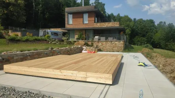 <p>Zde je vidět příkladná ukázka toho, jak designové zastřešení Slide Wood spojuje celý koncept zahrady a rodinného domu. Zastřešení je tvořeno ze dvou dílů, přičemž menší díl zajíždí do většího dílu a oba díly se odsunou za hranu bazénu. Na povrch zastřešení se použily přírodní dřevěná terasová prkna, která se ukazují taktéž na fasádě domu. Přirozenou přírodní atmosféru podtrhává kámen kolem terasy u bazénu.</p>
